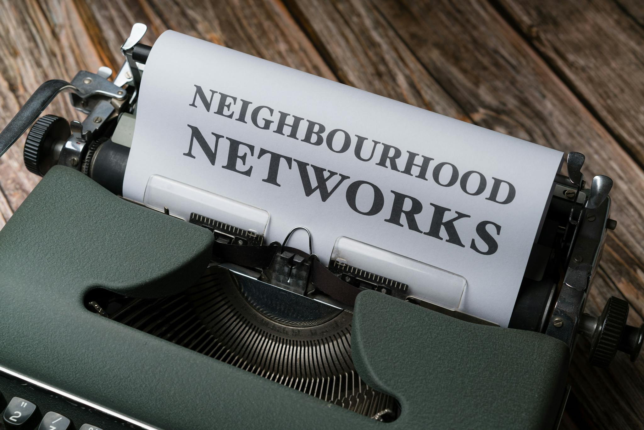 A vintage typewriter displaying the text 'Neighbourhood Networks' on a wooden desk.